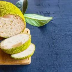 Un árbol de pan cortado, mostrando su interior blanco y esponjoso, junto a unas hojas verdes sobre una tabla de madera.